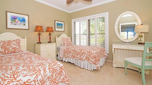 A bedroom with two beds, a ceiling fan, a desk with a chair, and a large window with shutters. - Georgetown Villas #113 on Seven Mile Beach & Pool (George Town)