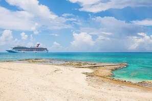 Ein Kreuzfahrtschiff liegt vor einem Strand mit klarem türkisblauem Wasser und sandigem Ufer.