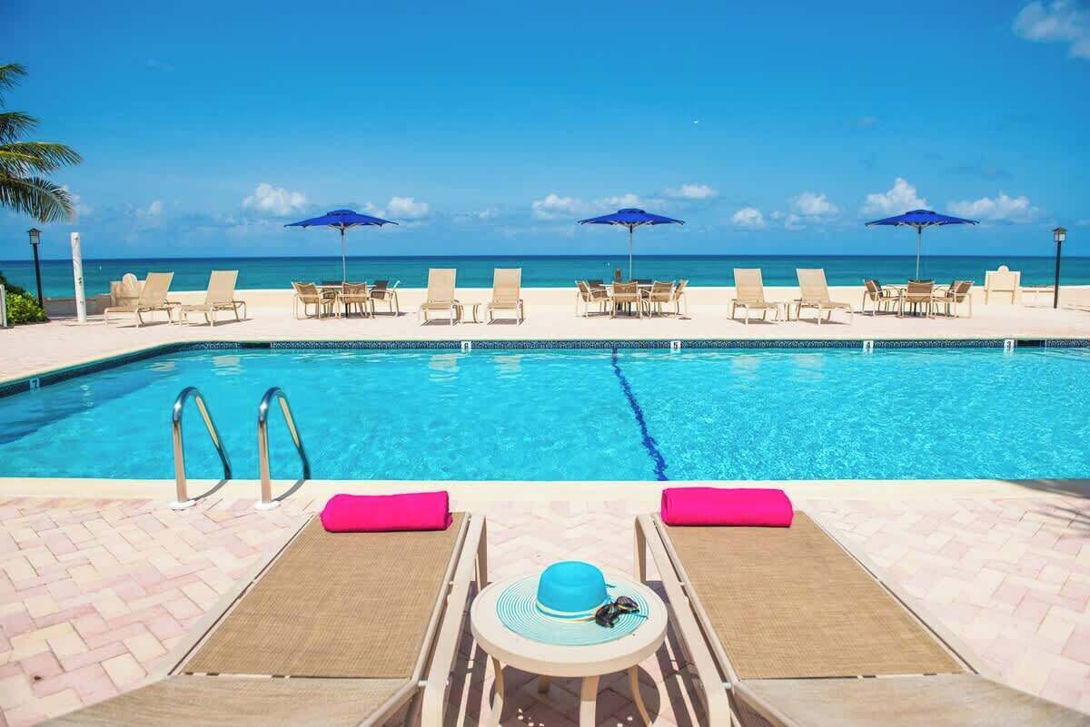 Uma área à beira da piscina com espreguiçadeiras e guarda-sóis, uma piscina azul límpida e vista para o mar.