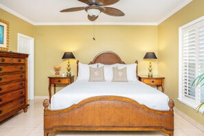 Une chambre à coucher avec un grand lit, deux tables de chevet avec des lampes, une commode et un ventilateur de plafond.