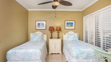 A bedroom with two beds, a ceiling fan, a nightstand with lamps, and a window with blinds.