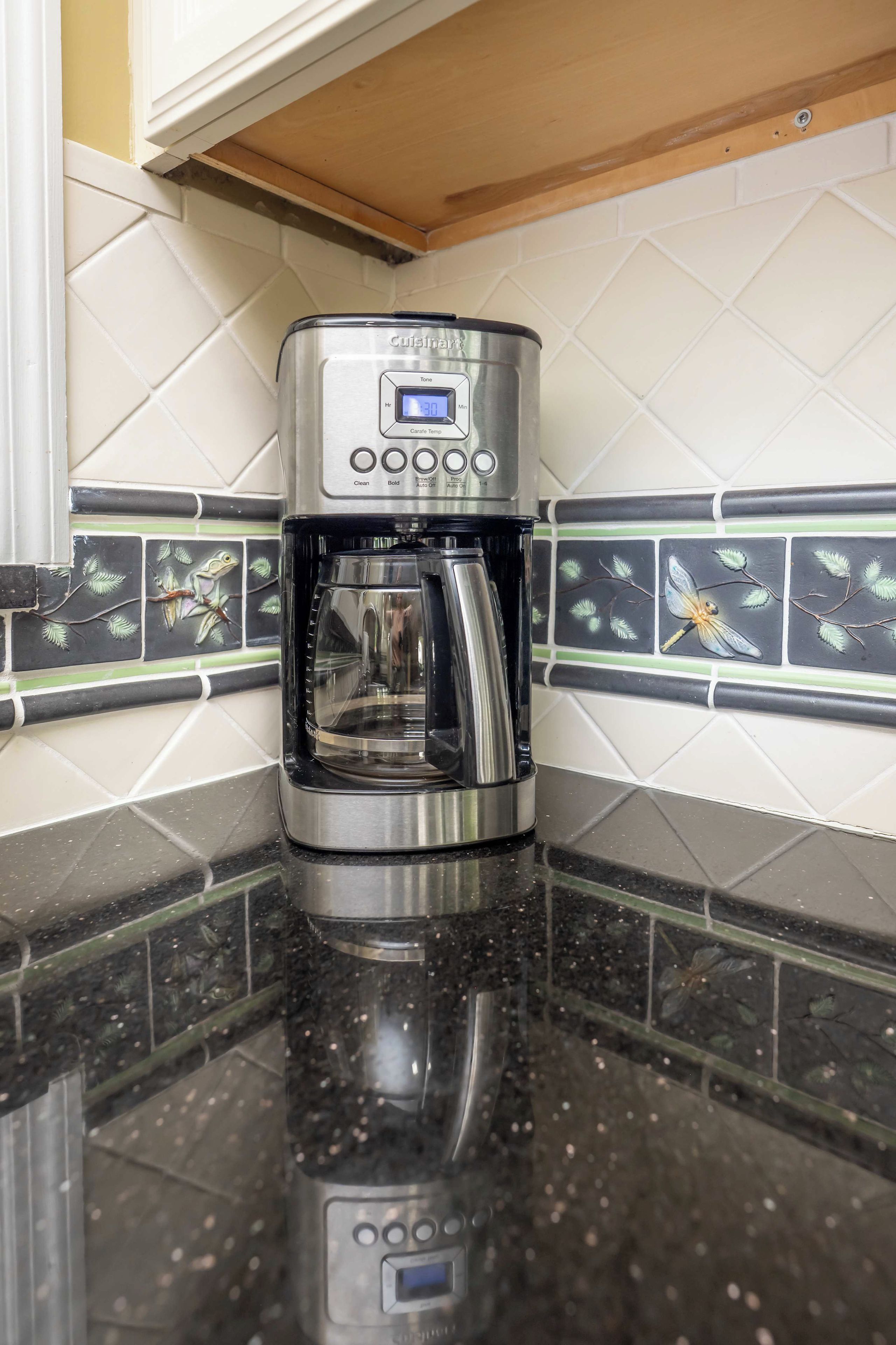 A coffee maker on a kitchen counter with a tiled backsplash.