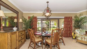 A dining area with a round table, four chairs, a chandelier, and a large mirror. - Georgetown Villas #113 on Seven Mile Beach & Pool (George Town)