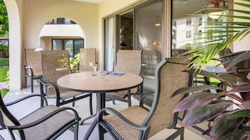 An outdoor patio area with a round table and chairs, a glass door leading to a covered entrance, and a view of a building in the background.