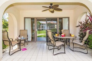 Eine überdachte Terrasse mit Tisch und Stühlen, einem Deckenventilator und Blick durch Glastüren in einen Garten.