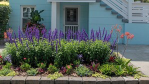 A two-story building with a balcony, a staircase, and a flower bed in front. - DownStairs with Great back yard for kiddos (Folly Beach)