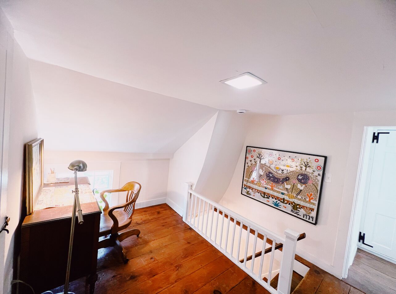 A room with a desk, chair, and a painting on the wall.