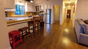 A kitchen with wooden flooring, white cabinets, a stainless steel refrigerator, and a dining area with stools.