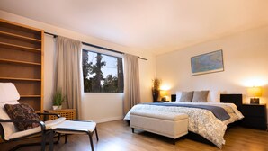 A bedroom with a bed, bedside tables, a chair, a desk, and a window with curtains.