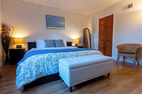 Un dormitorio con una cama grande, dos mesitas de noche con lámparas, un armario de madera y una silla de mimbre.