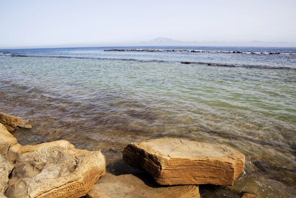 A rocky shoreline with clear water and distant mountains.