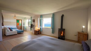 Une chambre avec un grand lit, un plancher en bois, une cheminée, un canapé et une vue sur la mer.