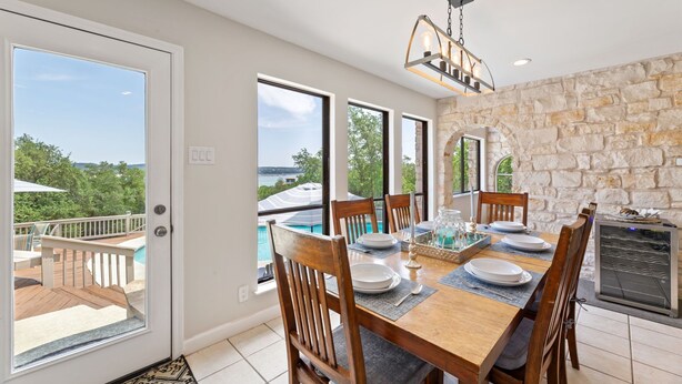 A dining area with a stone wall, large windows, and a view of a pool. - Lake Travis Oasis, Pool, Hot Tub, Lake Views, Near Marinas & Austin! (Austin)