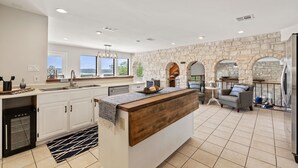 A modern kitchen with a stone accent wall, a central island, and a view of the outdoors. - Lake Travis Oasis, Pool, Hot Tub, Lake Views, Near Marinas & Austin! (Austin)