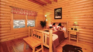A log cabin room with a wooden bed, a wooden chair, a small table, a nightstand, and a window with a view of the outdoors. - Mountain top overlooking lake, Hot Tub, Pickleball, Yukon Fire Pit, 5 STAR, PETS (Waleska)
