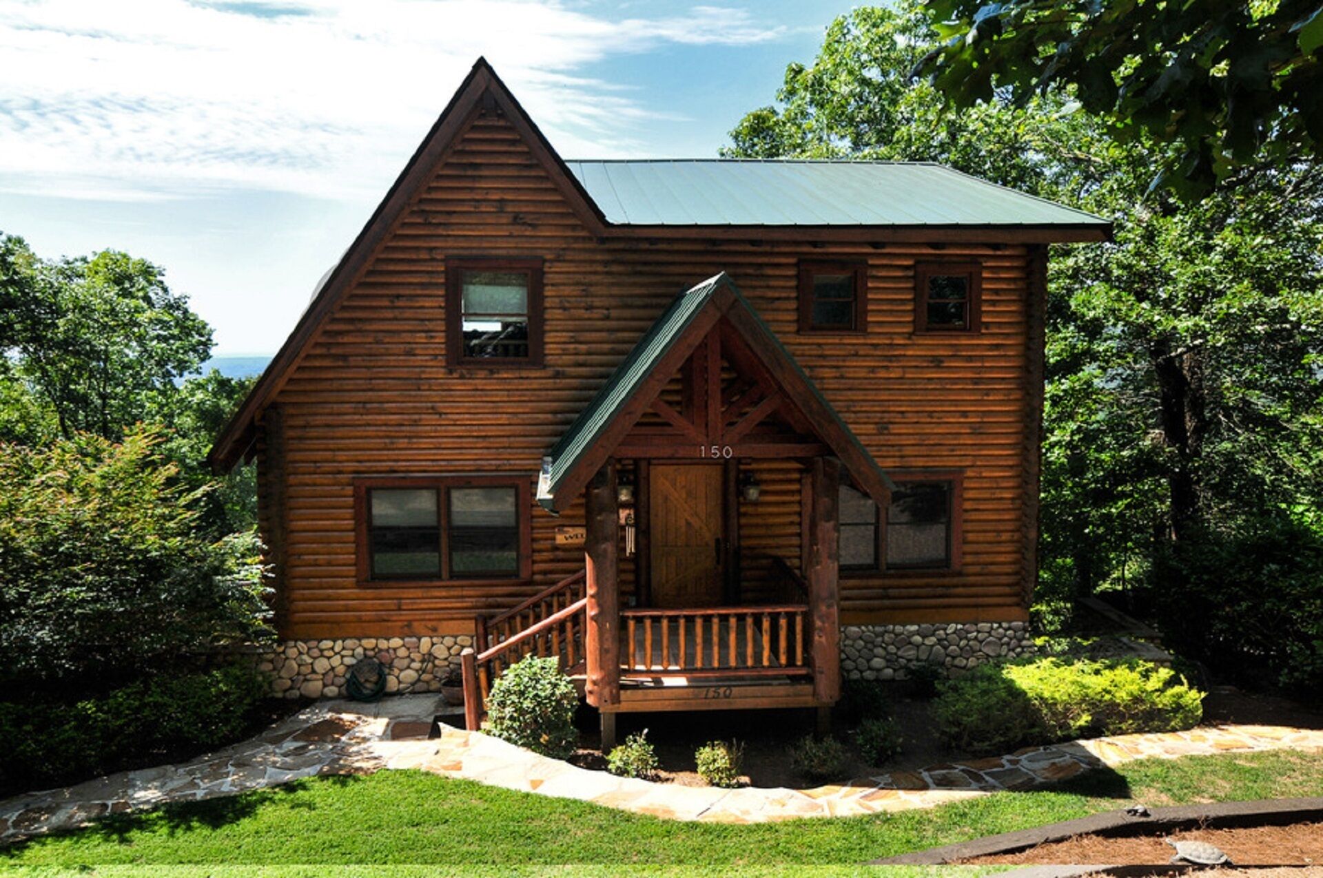 A log cabin with a stone foundation, a wooden porch, and a number '150' displayed on the front.