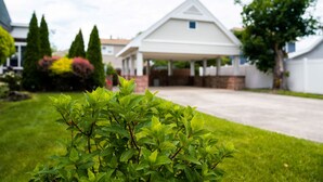 A residential house with a covered driveway, a lawn, and a variety of trees and shrubs.