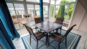 A covered patio with a table and chairs, large windows, and a view of the backyard.