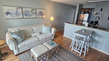 A compact living space with a sofa, a small table, a bench, and a kitchen area.