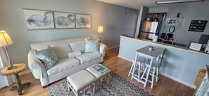 A compact living space with a sofa, a small table, a bench, and a kitchen area.