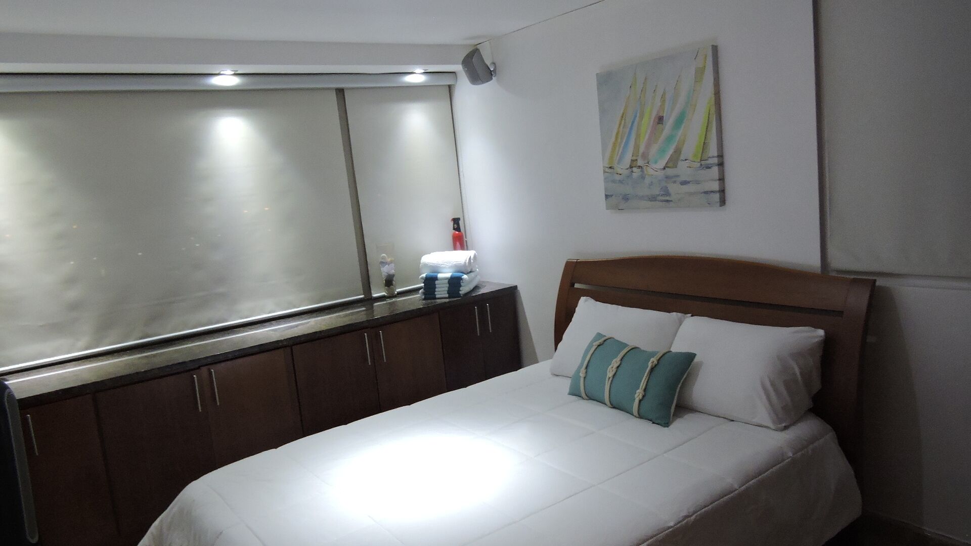 A bedroom with a bed, a wooden headboard, a nightstand, a mirror, and a painting of sailboats.