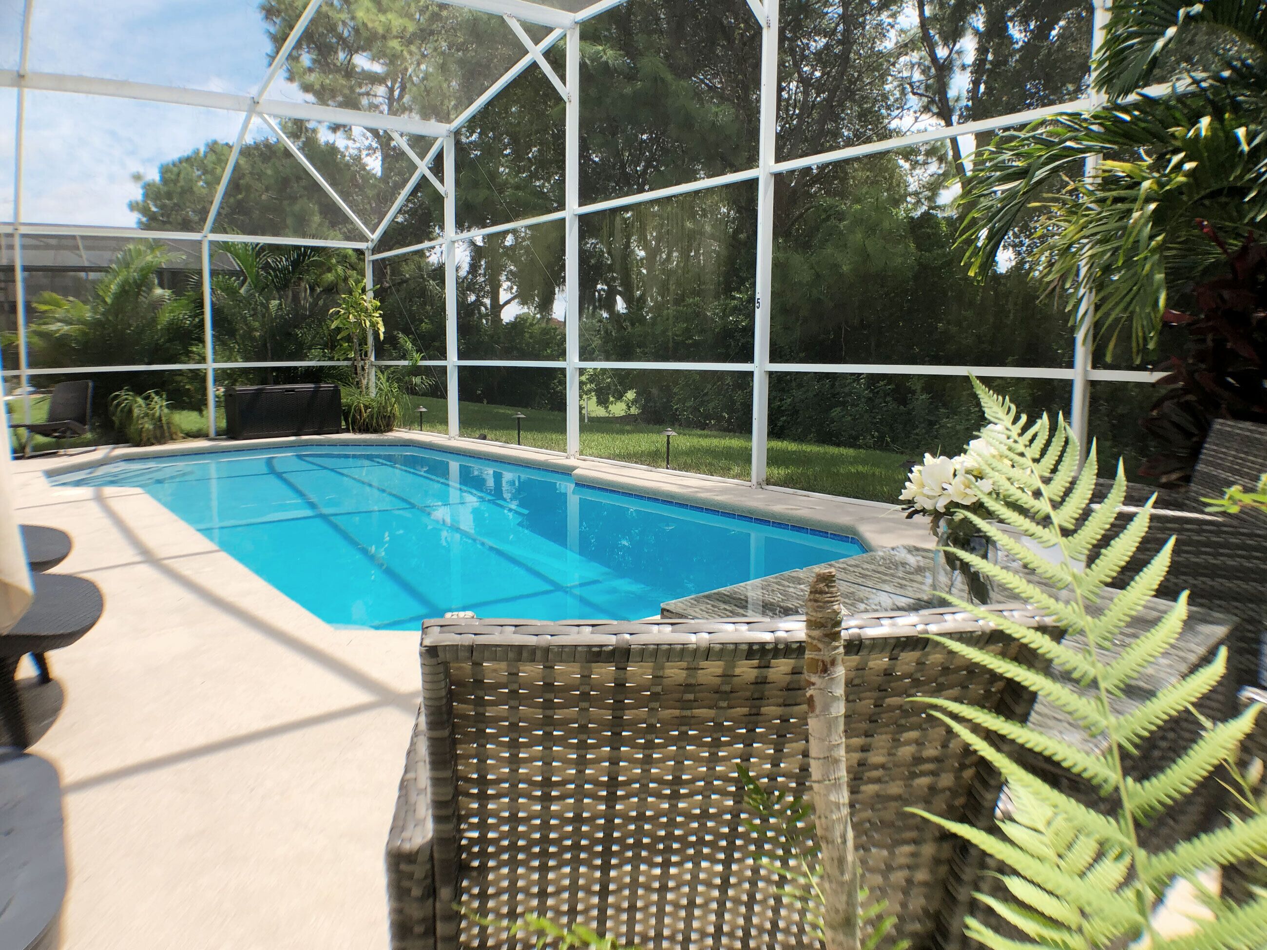 A swimming pool with a glass enclosure, surrounded by greenery and outdoor furniture.