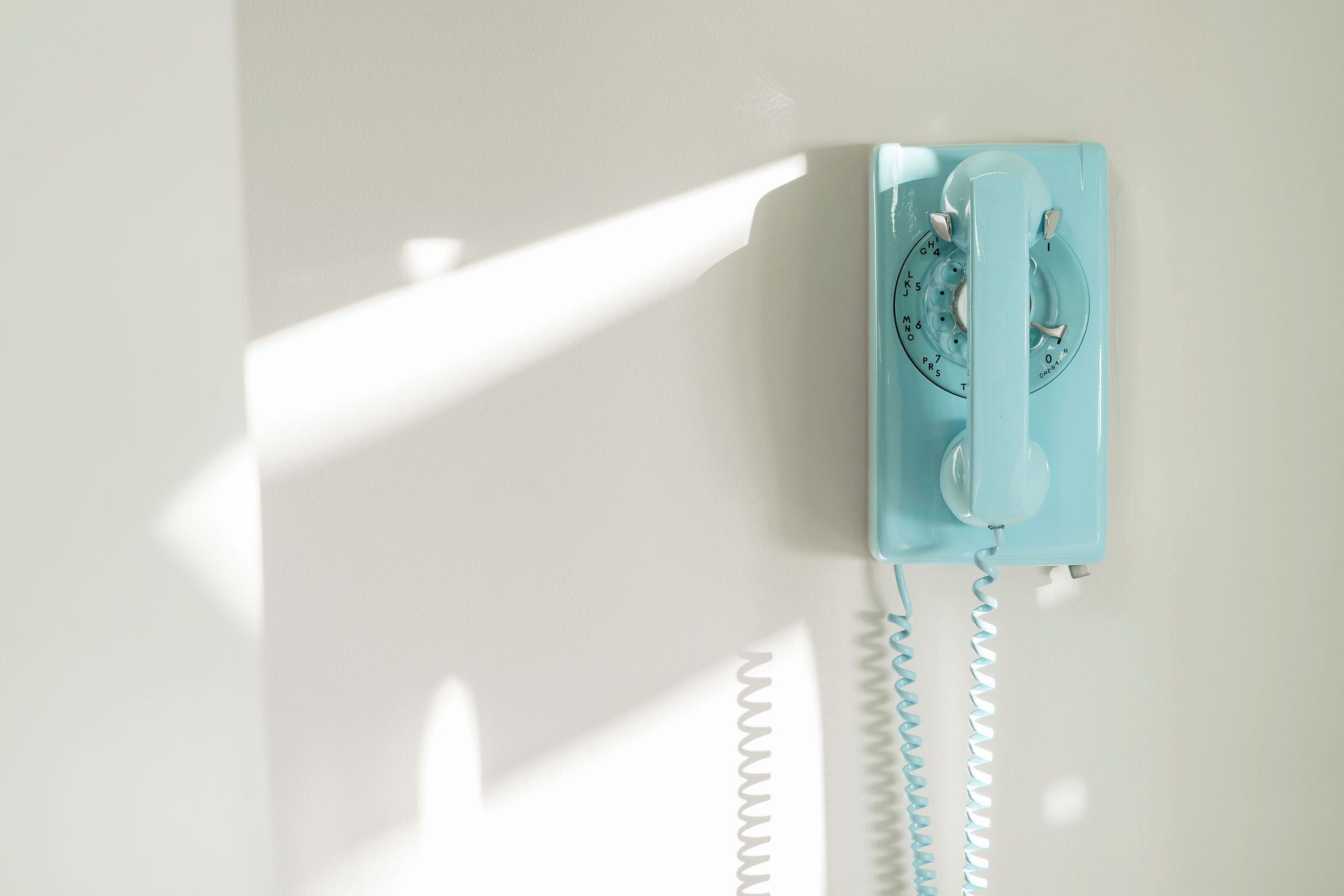 Un téléphone à cadran rotatif bleu clair, fixé à un mur blanc.