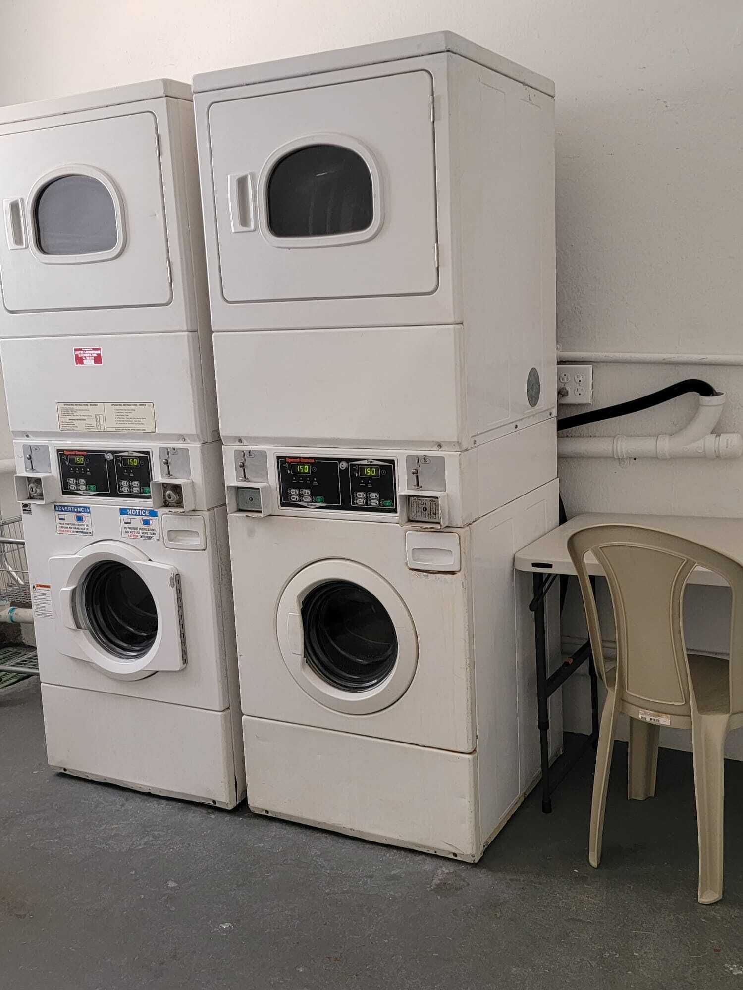 Pile di lavatrici bianche con pannelli di controllo e una sedia di plastica.
