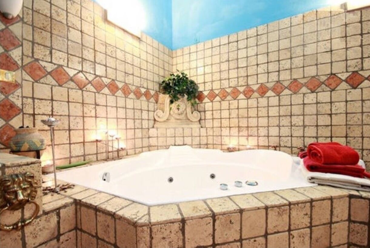 A bathroom with a large bathtub, tiled walls, and a decorative plant.
