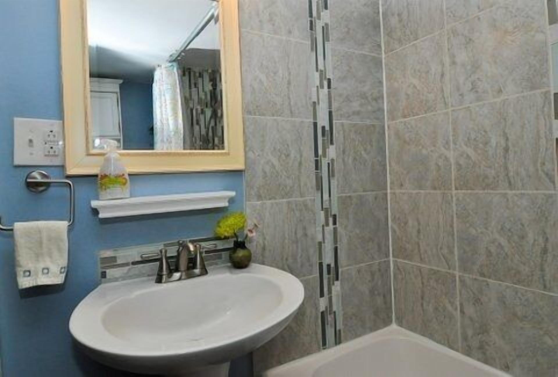 A bathroom with a sink, mirror, and shower area.