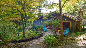 A rustic cabin with a stone pathway leading to a wooden deck, surrounded by lush greenery and trees. - Sweet Cabin in the Woods -10 min to Ashvl., Quiet, BEES , Garden & DECK. Dogs Ok (Asheville)
