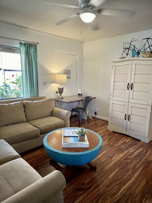 A living room with a sofa, a coffee table with a tray, a desk with a chair, and a white cabinet.