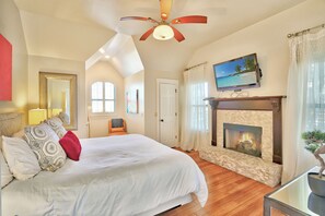 A spacious bedroom with a large bed, a fireplace, and a ceiling fan. - Romantic-amazing Views-Newly Renovated-new Hot Tub-has It All! (Wimberley)