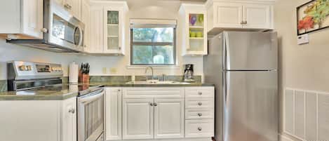 A kitchen with white cabinets, stainless steel appliances, a window, and a vent on the wall.