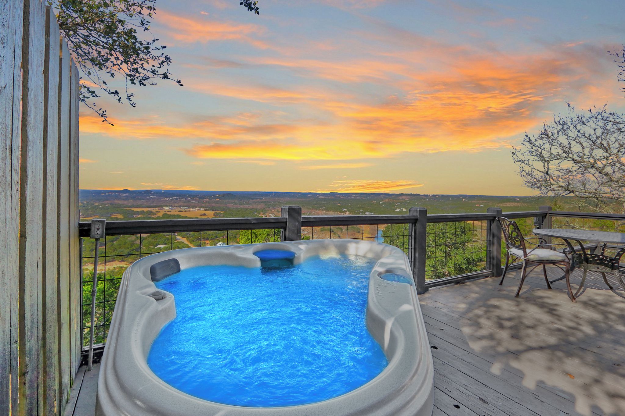 A hot tub on a wooden deck with a view of the landscape and a sunset.