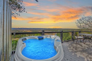 A hot tub on a wooden deck with a view of the landscape and a sunset.