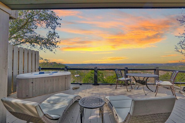 A deck with outdoor seating, a hot tub, and a scenic view of the sunset.