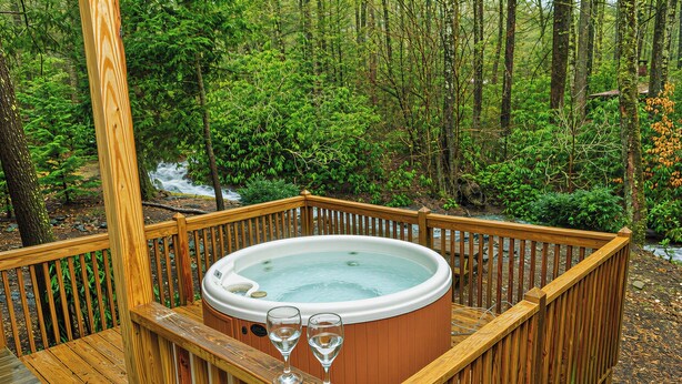 Een hottub op een houten terras, omringd door een bos.