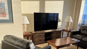Ein Wohnzimmer mit einer Ledersofa, einem Holztisch, einem Flachbildfernseher und einer Lampe auf einem Beistelltisch.