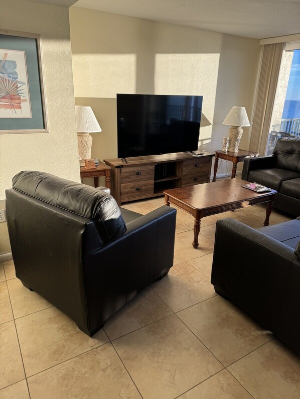 A living room with a leather sofa, a wooden coffee table, a flat-screen TV, and a lamp on a side table.