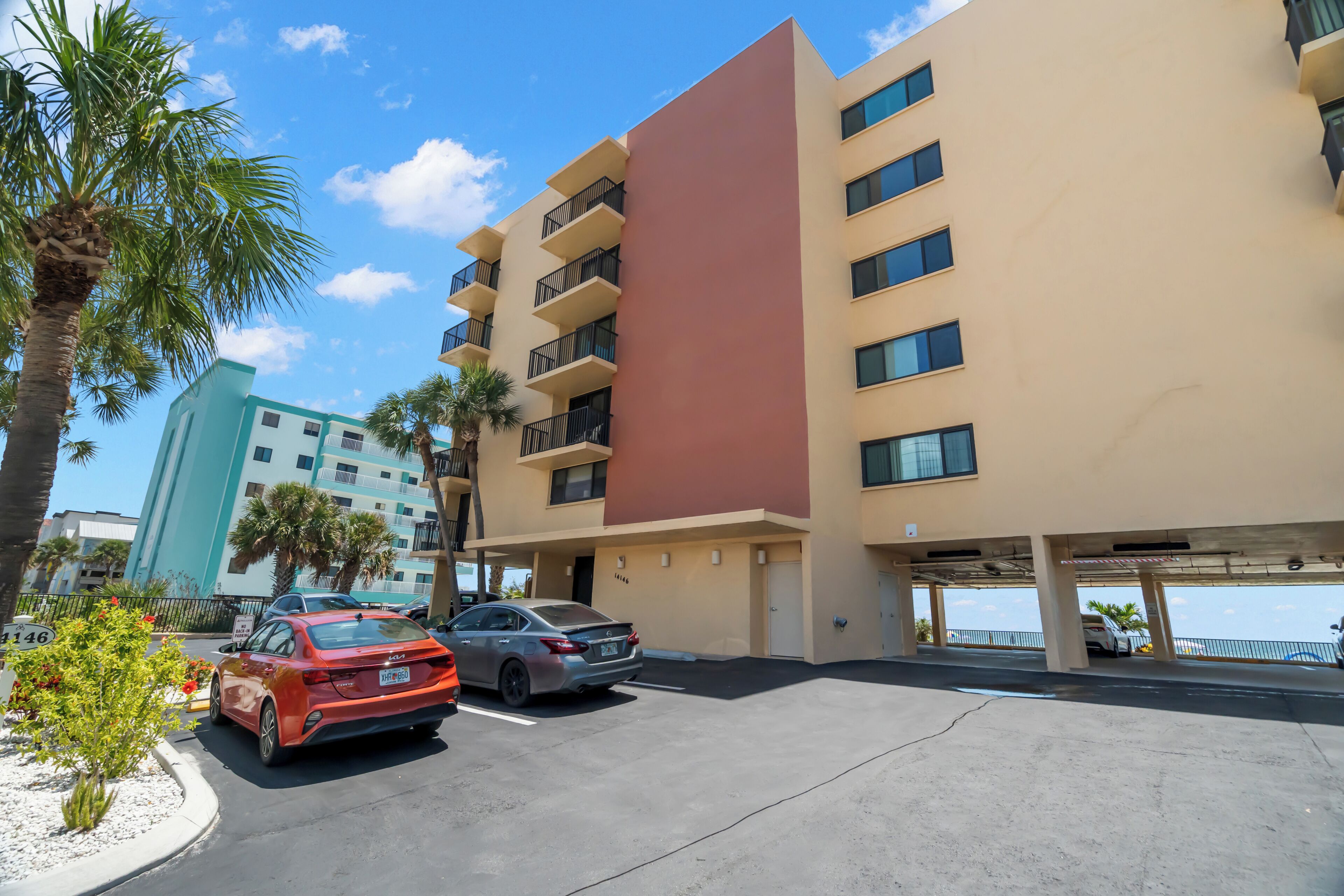 A multi-story hotel with a parking garage, palm trees, and a clear sky.