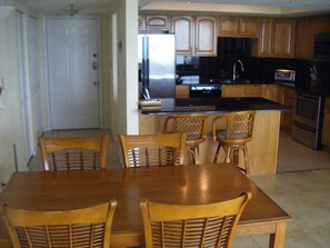 A kitchen with wooden cabinets, a stainless steel refrigerator, a microwave, and a stove. There is a dining table with four chairs.