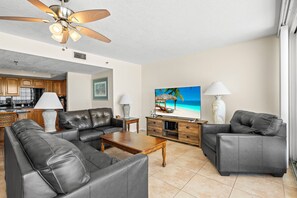 A living room with a sofa, coffee table, TV, and a ceiling fan. - Special Rates for Nov 21 - Dec 19, 2026 - All Rooms Directly Beach Front (Madeira Beach)