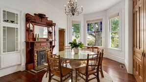 Une salle à manger avec une table ronde en verre, des chaises en bois, un lustre et une cheminée agrémentée d’un miroir.
