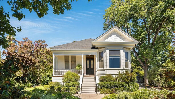 Une maison à deux étages avec un porche à l’avant, un petit jardin et un chemin menant à la porte d’entrée.