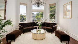 Un salon avec une table basse ronde en verre, deux canapés marron, un tapis blanc et une grande fenêtre donnant sur des arbres et des immeubles.
