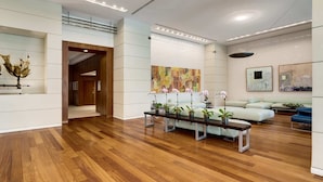 Un hall d’entrée spacieux avec un plancher en bois, un comptoir de réception, un coin salon avec des canapés et un grand tableau abstrait accroché au mur.