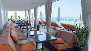 Un espace extérieur lumineux, aménagé avec des canapés confortables et des tables, offrant une vue sur une piscine et la mer.
