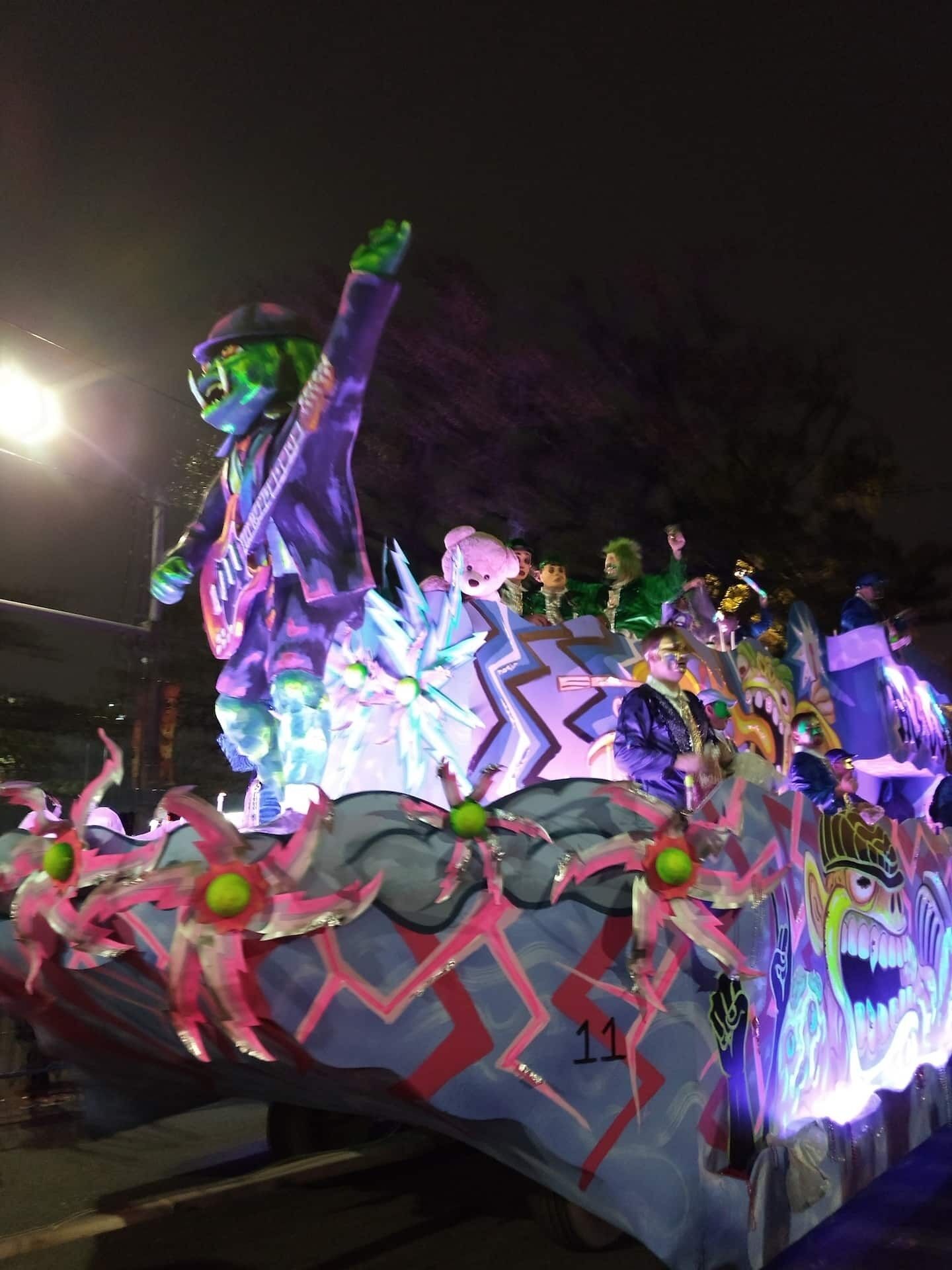 Un carro colorido con diversas figuras y decoraciones, incluyendo una figura con sombrero verde y otra con sombrero púrpura.