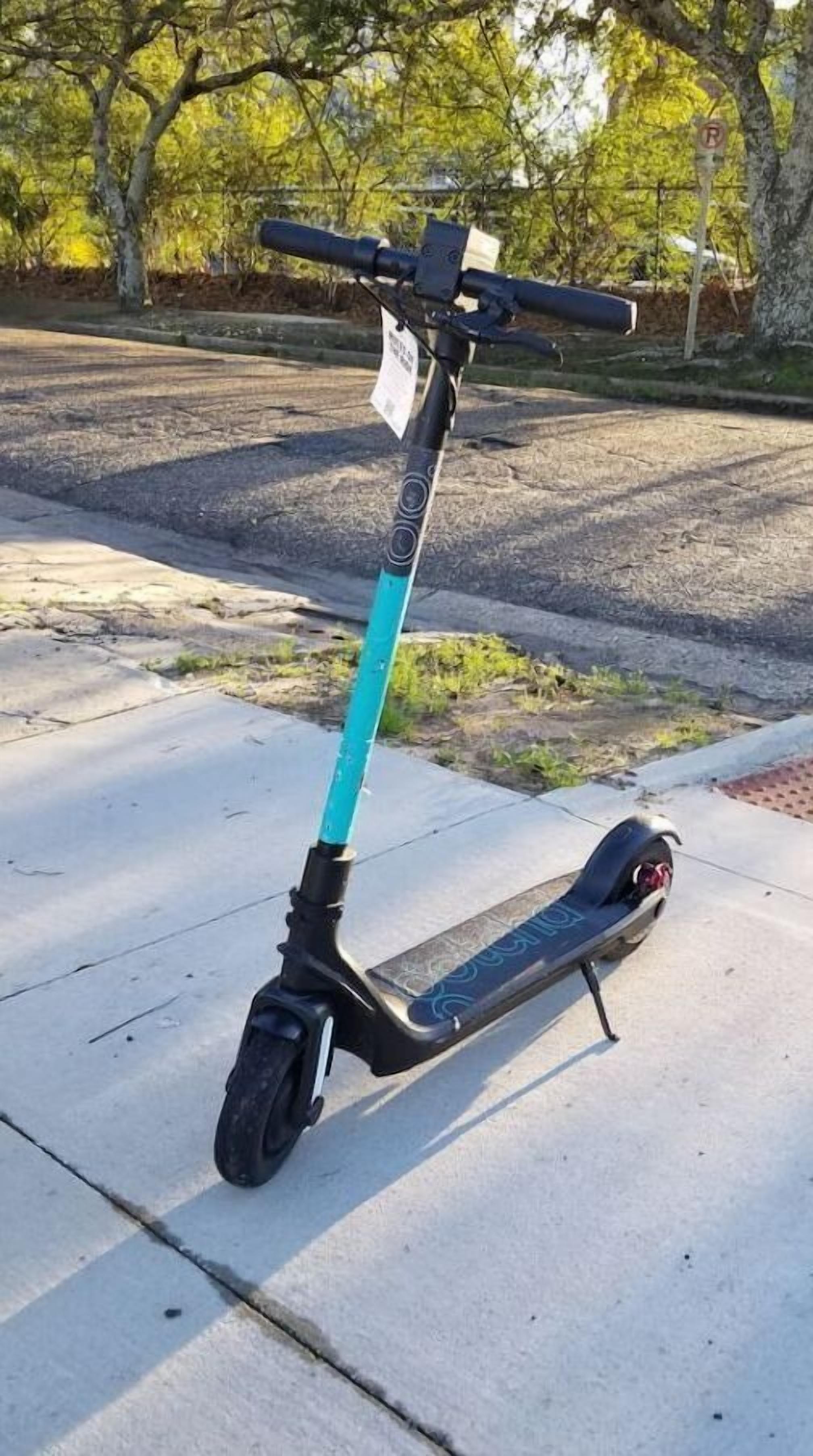 Ein stehender Roller mit türkisfarbenem Lenker und schwarzem Sitz, auf einer Betonfläche geparkt.